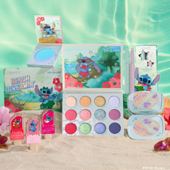 Disney Lilo and Stitch Collection by ColourPop Full Collection Set displayed on sandy beach - 12-pan Beach Dreaminβ eyeshadow palette, lip gloss trio, two cream gel liners, marbled highlighter compact, and jelly highlighter in tropical Stitch packaging.