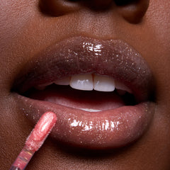 Close-up of glossy, glittering lips being coated with Beautiful Belle Belle Lip Mask & Ultra Glossy Lip applicator in a shimmery pink shade, showcasing Disney Princess inspired makeup detail for US beauty shoppers.