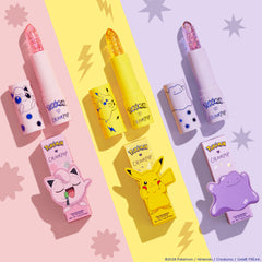 Thunderbolt, a ColourPop pH Lip Balm featuring Pikachu, stands uncapped with a sparkly gold translucent bullet; bright yellow tube and matching box centered on a pastel yellow stripe, flanked by pink and purple character balms with star and lightning motifs.