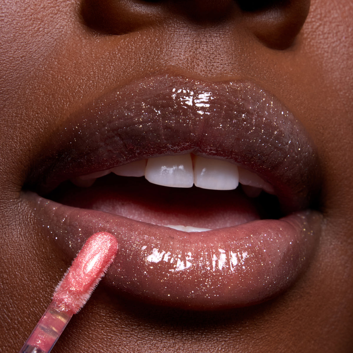Close-up of glossy, glittering lips being coated with Beautiful Belle Belle Lip Mask & Ultra Glossy Lip applicator in a shimmery pink shade, showcasing Disney Princess inspired makeup detail for US beauty shoppers.