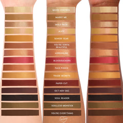 ColourPop New Moon Shadow Palette swatches stripe three skin tones, showing warm golds, coppers, reds, browns, black and olive in matte and shimmer finishes, with shade names like Mood Control, Marry Me, Adrenaline, Bloodsuckers, and You’re Everything.