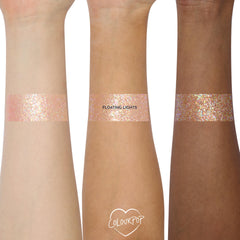 Floating Lights ColourPop Glitter Gel swatched in wide bands on three forearms, showing iridescent pink-lavender and gold multi-size glitter in a sheer gel base, demonstrating payoff across light, medium, and deep skin tones.