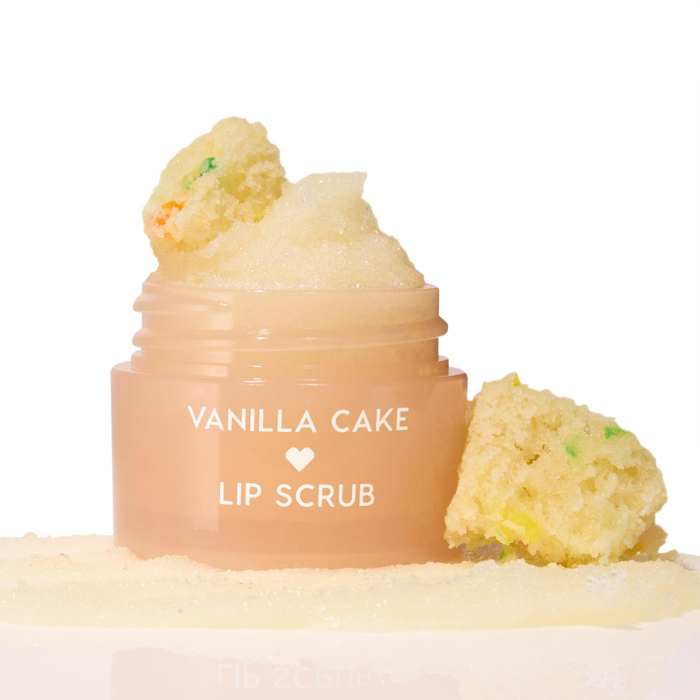 Vanilla Cake ColourPop Lip Scrub jar sits open, sugary scrub mounded on top and swatched at the base, flanked by funfetti cake crumbs on a clean white studio background.