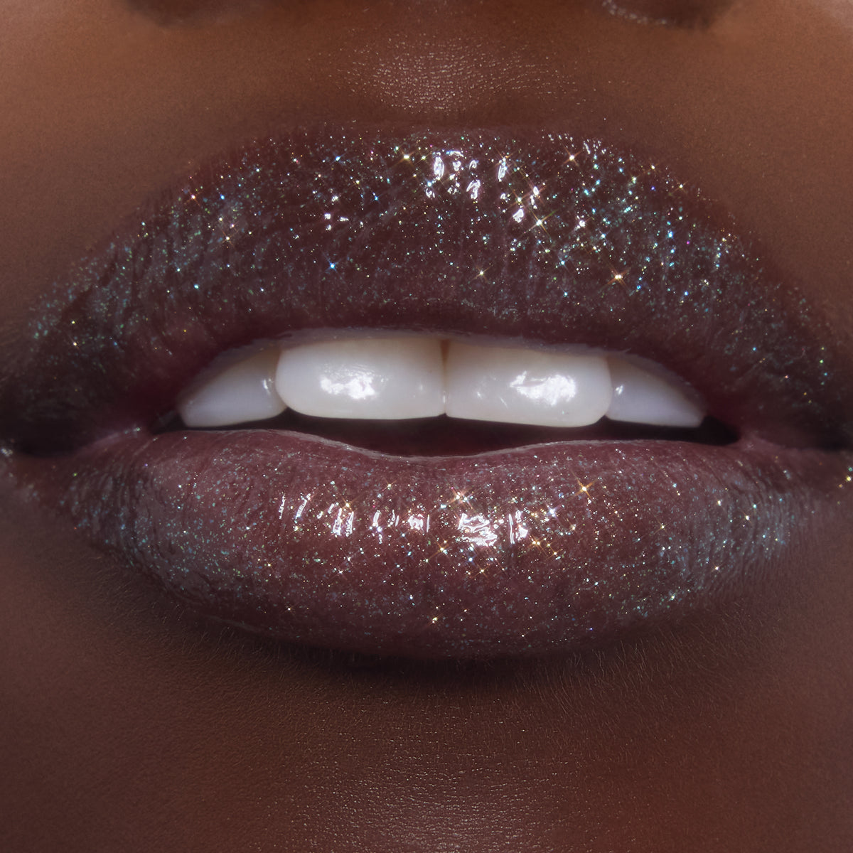 Lips wearing ColourPop Ultra Glossy Lip in Ogre, catching light with multi-dimensional shimmer and glassy shine as teeth gently show; studio macro highlights the deep plum base packed with fine glitter.