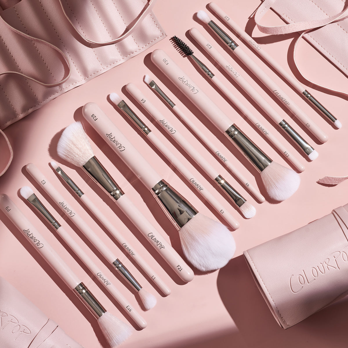 Smoke 'N Roses Brush Roll displaying a full ColourPop Makeup Brush Kit: pink-handled powder, blush, eyeshadow, angled liner, and spoolie brushes with silver ferrules, arranged in a flat lay beside a blush-pink roll-up case embossed ColourPop.