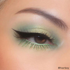 Sharp black wing defining a brown eye, created with ColourPop BFF Liquid Liner in Black, drawn along the upper lash line with a precise brush tip; shimmery mint and sage eyeshadow and green lower lashes complete the look.