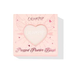 ColourPop Kiss 'N Tell pressed powder blush compact displays through a heart-shaped window in a pink box with winged-heart graphics, front-facing on a white background, 4.45g (0.16 oz) makeup packaging for US shoppers.